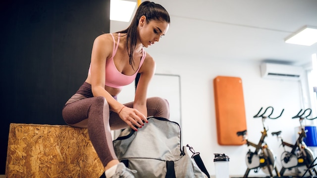 Mujer con ropa de deporte en el gimnasio revisando su bolsa deportiva