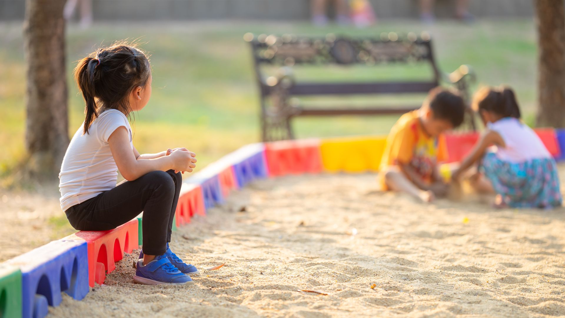 Niña sola observa a otros niños jugar en el parque