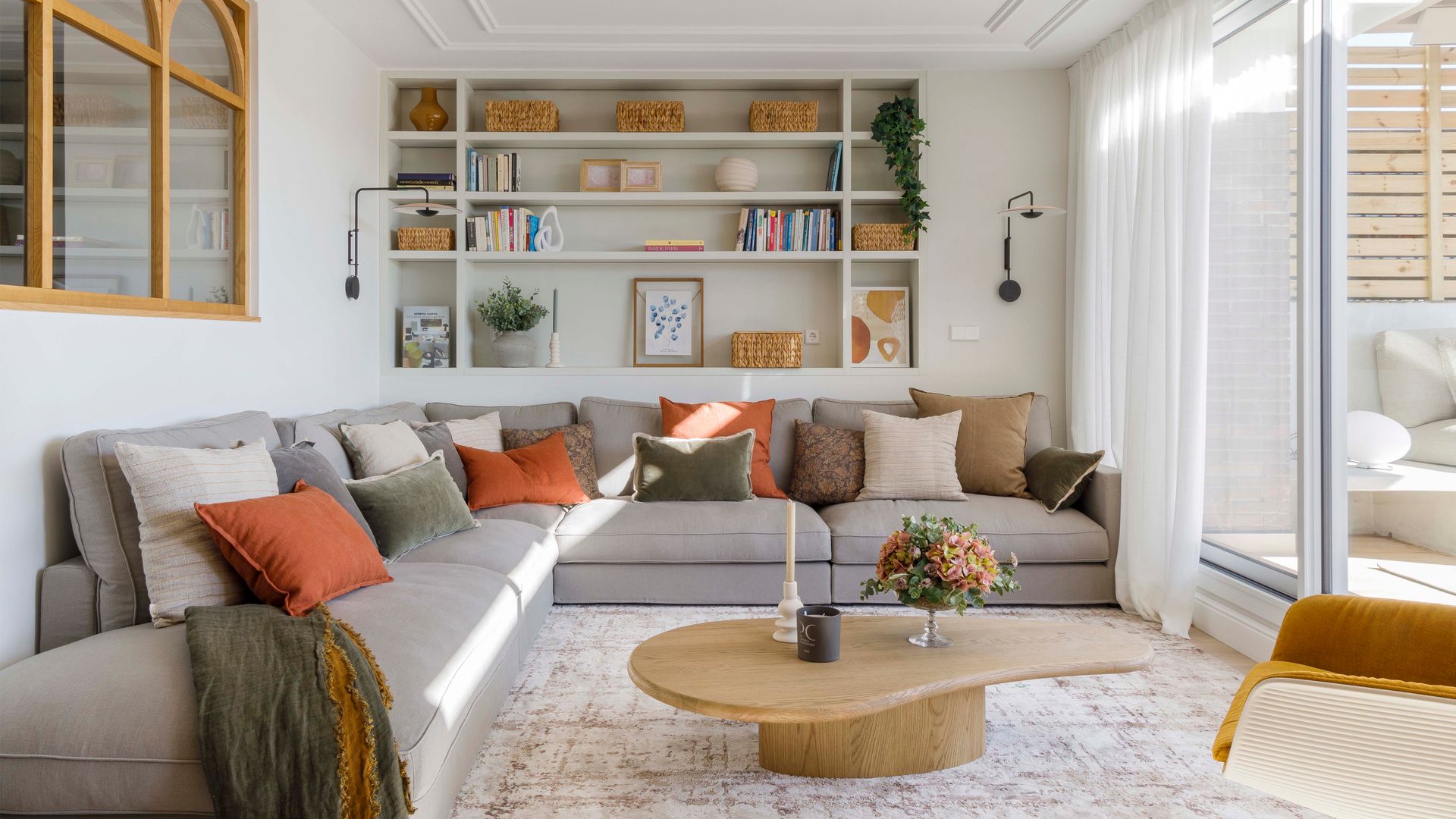 Salón con librería a medida en la pared del sofá, sofá gris en rincones, salida a la terraza, mesa de centro de madera, cojines en el sofá 