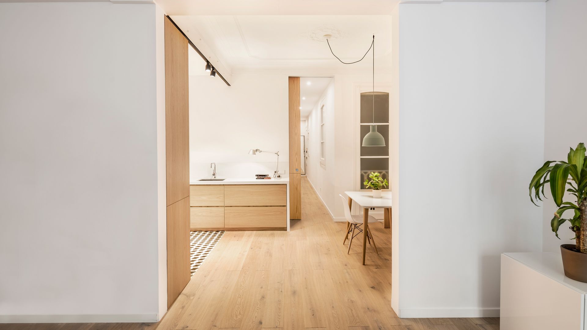 Cocina de madera con suelo de madera, puerta corredera, mesa de comedor blanco, lámpara de techo