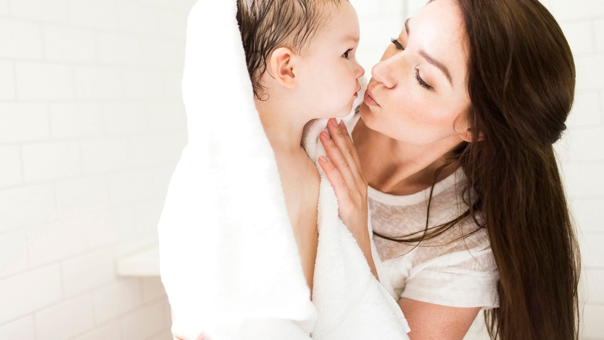 Madre dándole un beso a su bebé al salir de la ducha en el baño. El bebé está envuelto en una toalla blanca.