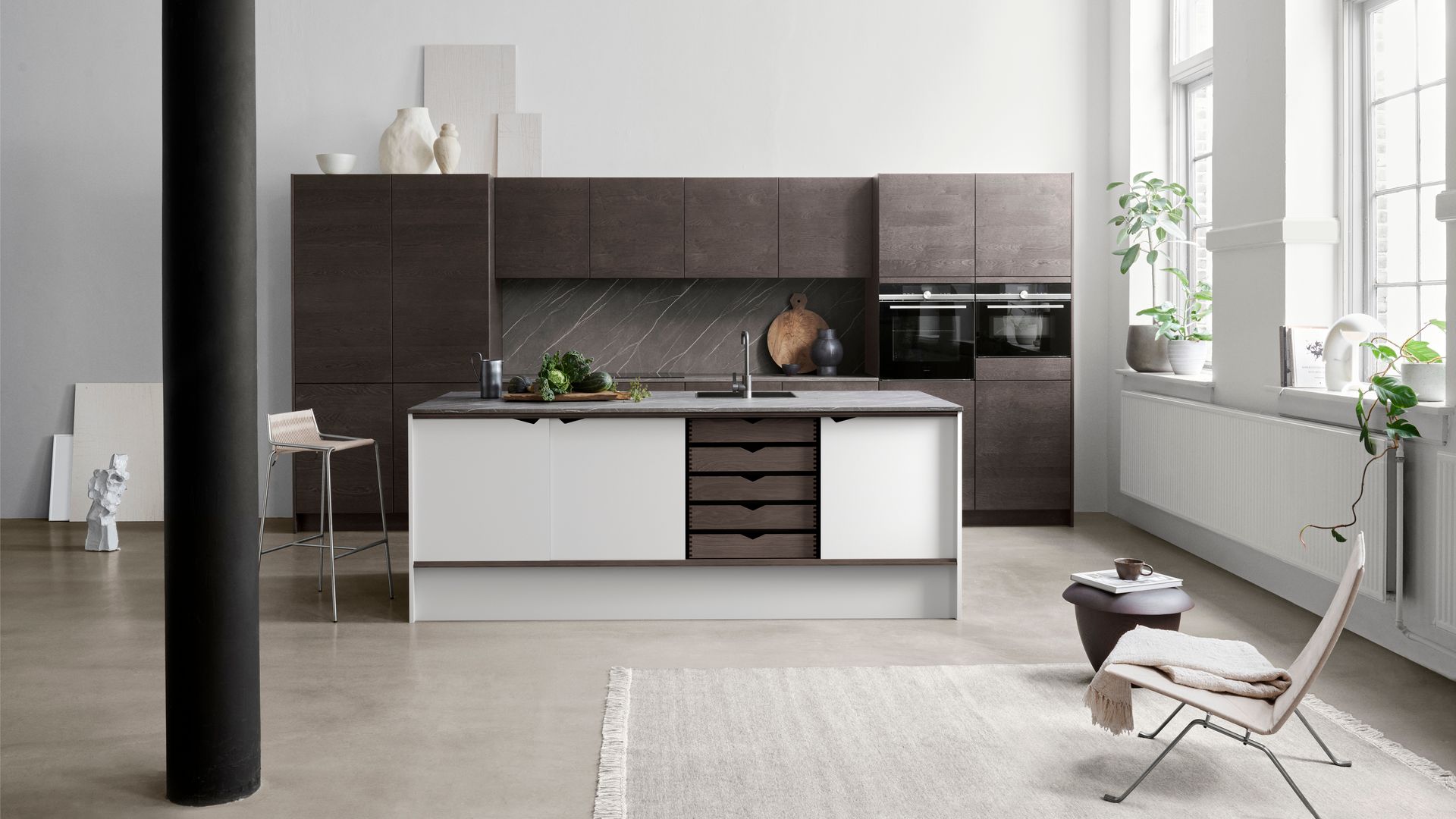 Cocina abierta con isla central, con armarios de madera oscura, grandes ventanales blanco, radiador bajo la ventana, alfombra, rincón de lectura