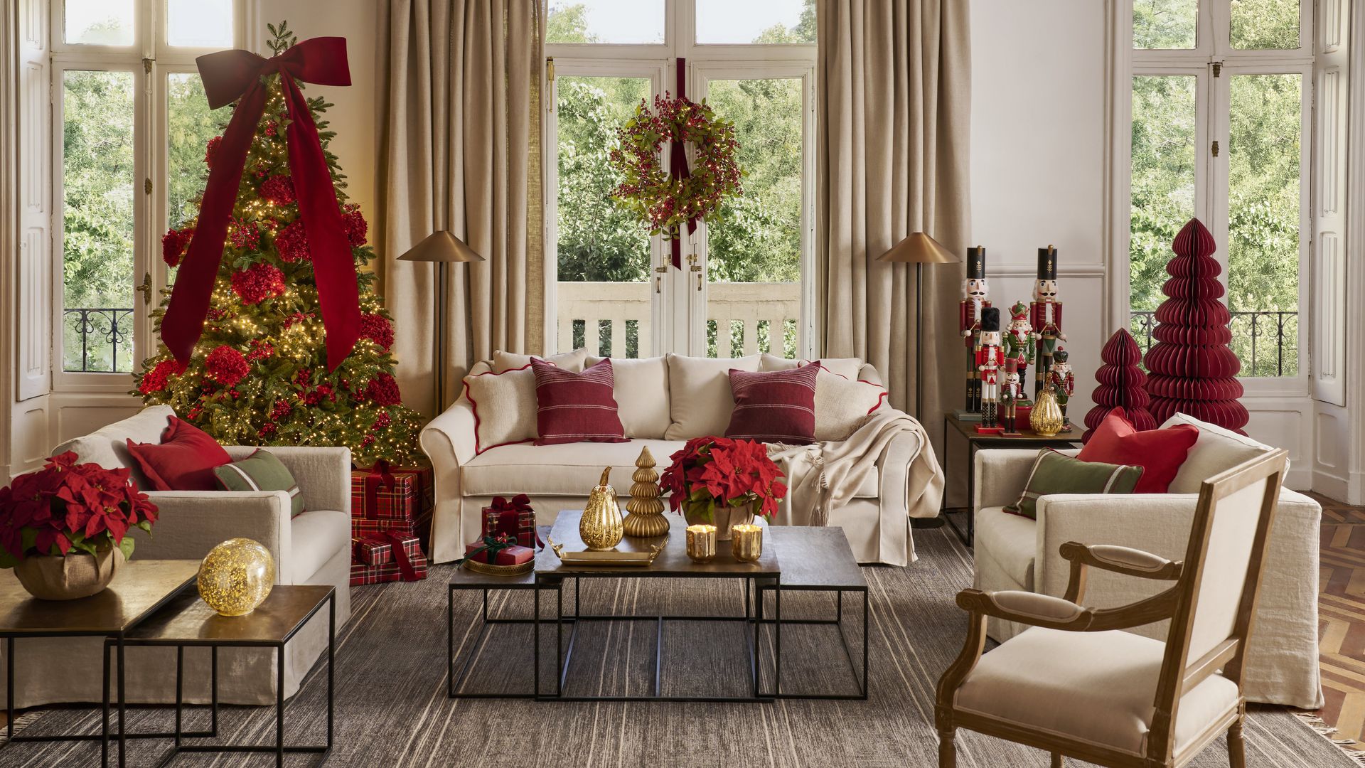 Salón decorado de Navidad, con árbol de Navidad con adornos rojos, gran lazo rojo, sofás beiges, alfombra, mesas de color negro, corona en la ventana, cojines rojos