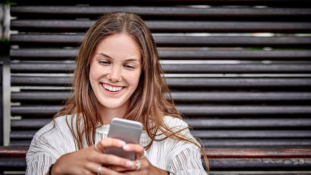 Happy young woman sitting at a bench looking at cell phone