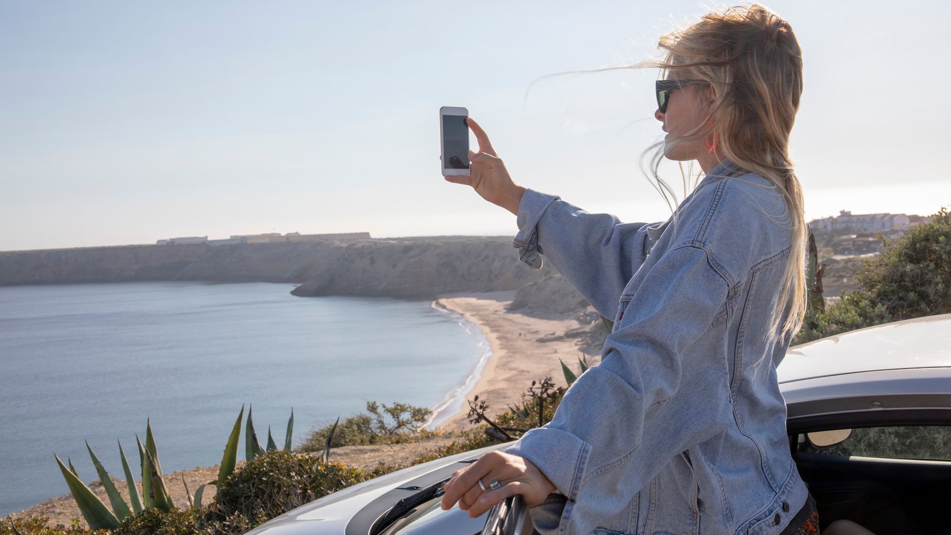 Chica joven tomando una fotografía con su teléfono móvil al Océano Atlántico desde su coche.