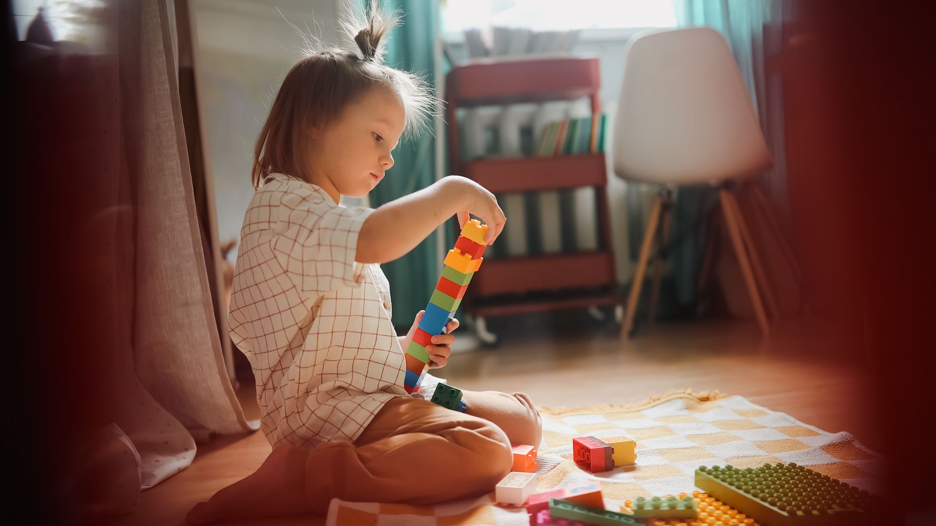 Niña jugando en el suelo de su casa con un juguete de construcciones, con una coleta en la cabeza.