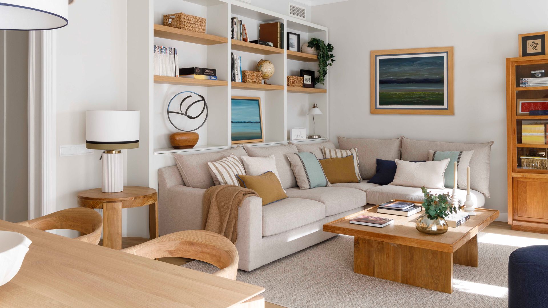 Salón comedor con sofá beige, estantería de obra, mesa de centro de madera, cojines en el sofá