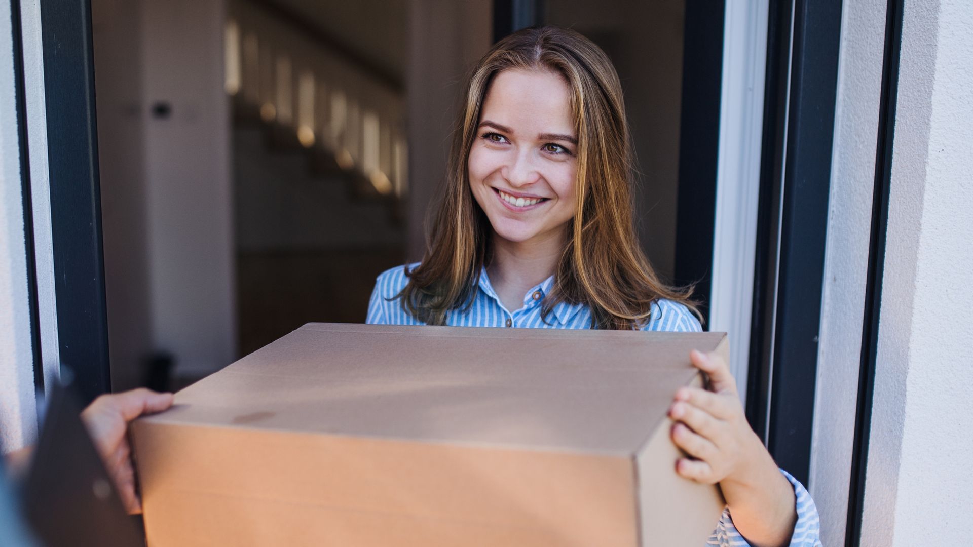 Mujer joven recogiendo una caja de manos de un repartidor en la puerta de su casa