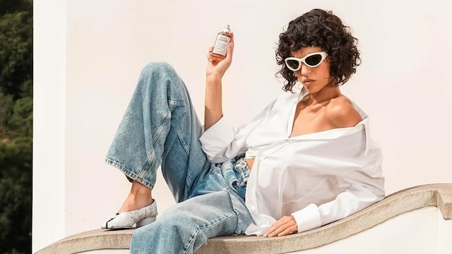Mujer morena con pelo rizado apoyada en un bordillo con perfume Replica de Maison Margiela