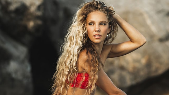 Mujer rubia con pelo largo ondulado sentada en una roca en el mar con conjunto rojo