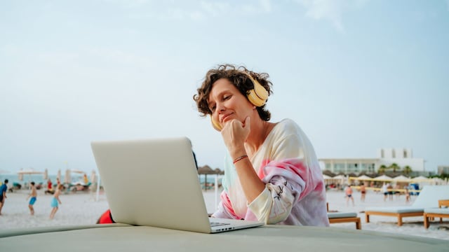 Una mujer en la playa con un portátil y unos auriculares 
