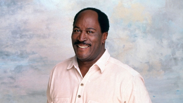 John Amos con las manos en los bolsillos sonriendo a cámara