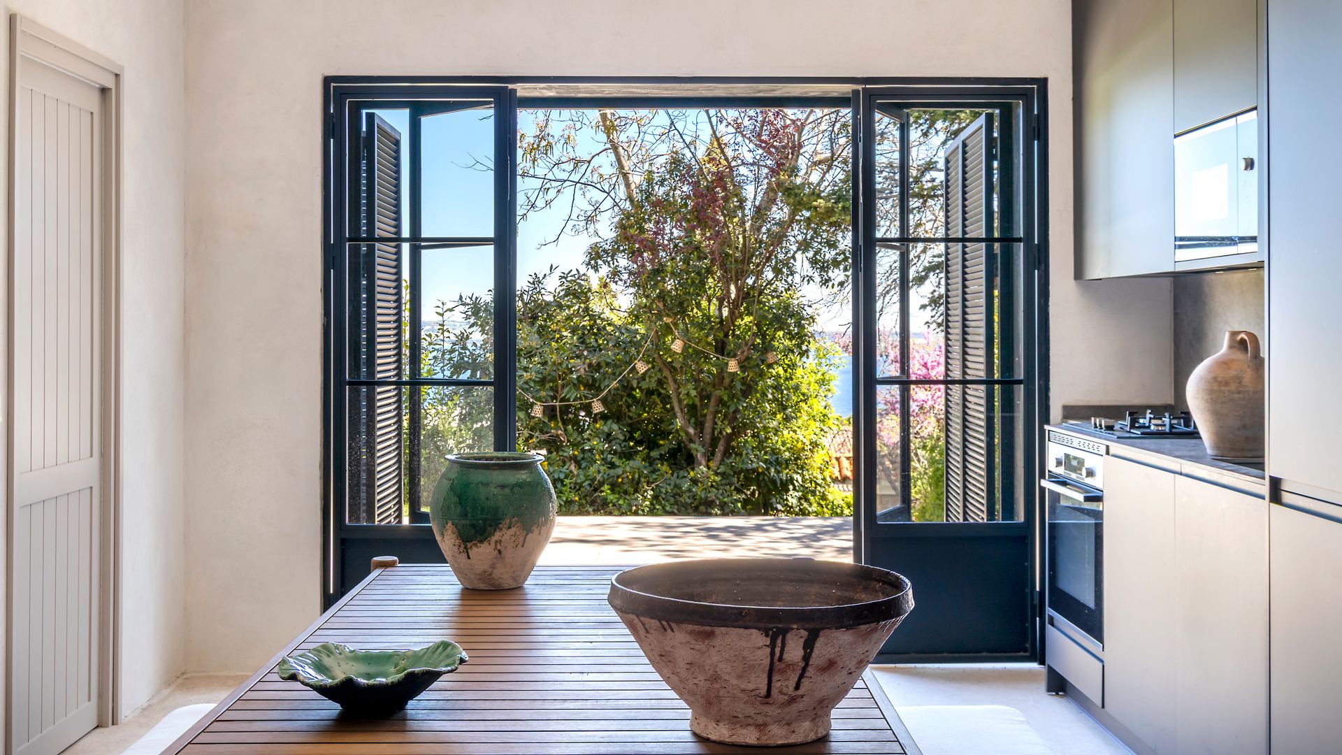 Cocina con salida al jardín con muebles blancos hasta el techo y mesa de cocina en el centro