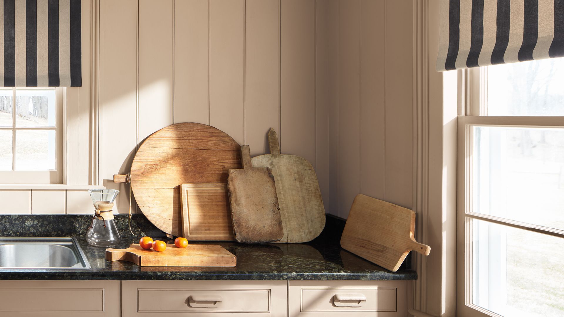 Cocina con lamas de madera beige, encimera de mármol negro, estores de rayas negras y beige