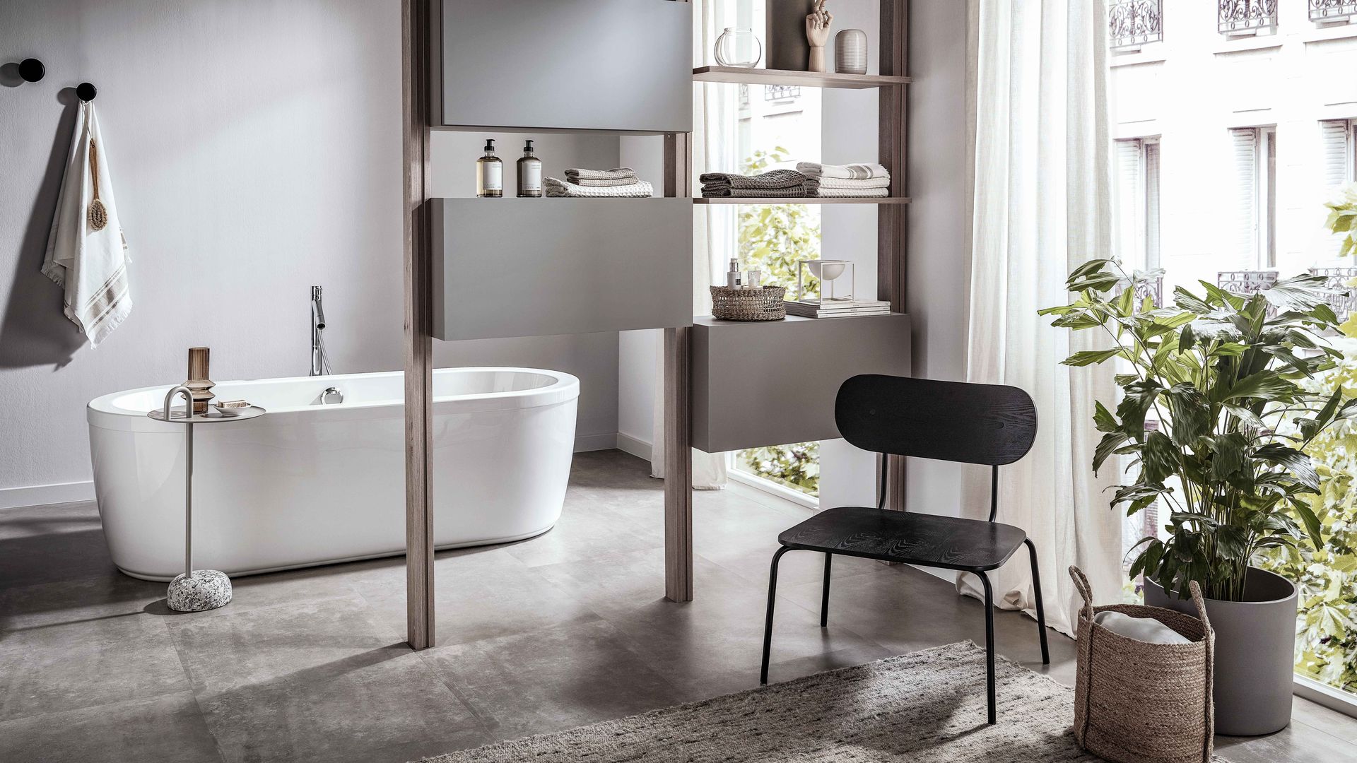 Baño con bañera exenta, estantería abierta, silla negra, alfombra, cestos y plantas
