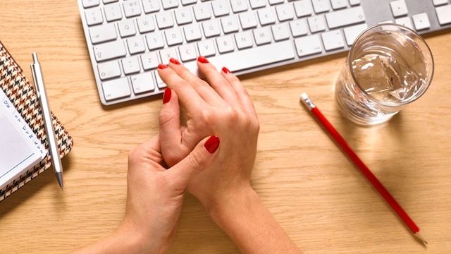 mujer tocándose las manos junto al teclado del ordenador