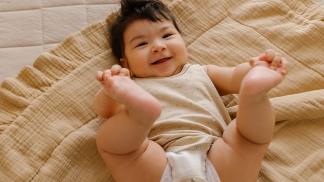 Niña bebé sonriendo en body y pañal, sobre una muselina en la cama