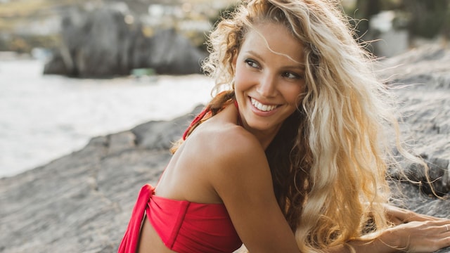 Mujer rubia bronceada con bikini rojo tumbada sobre una roca