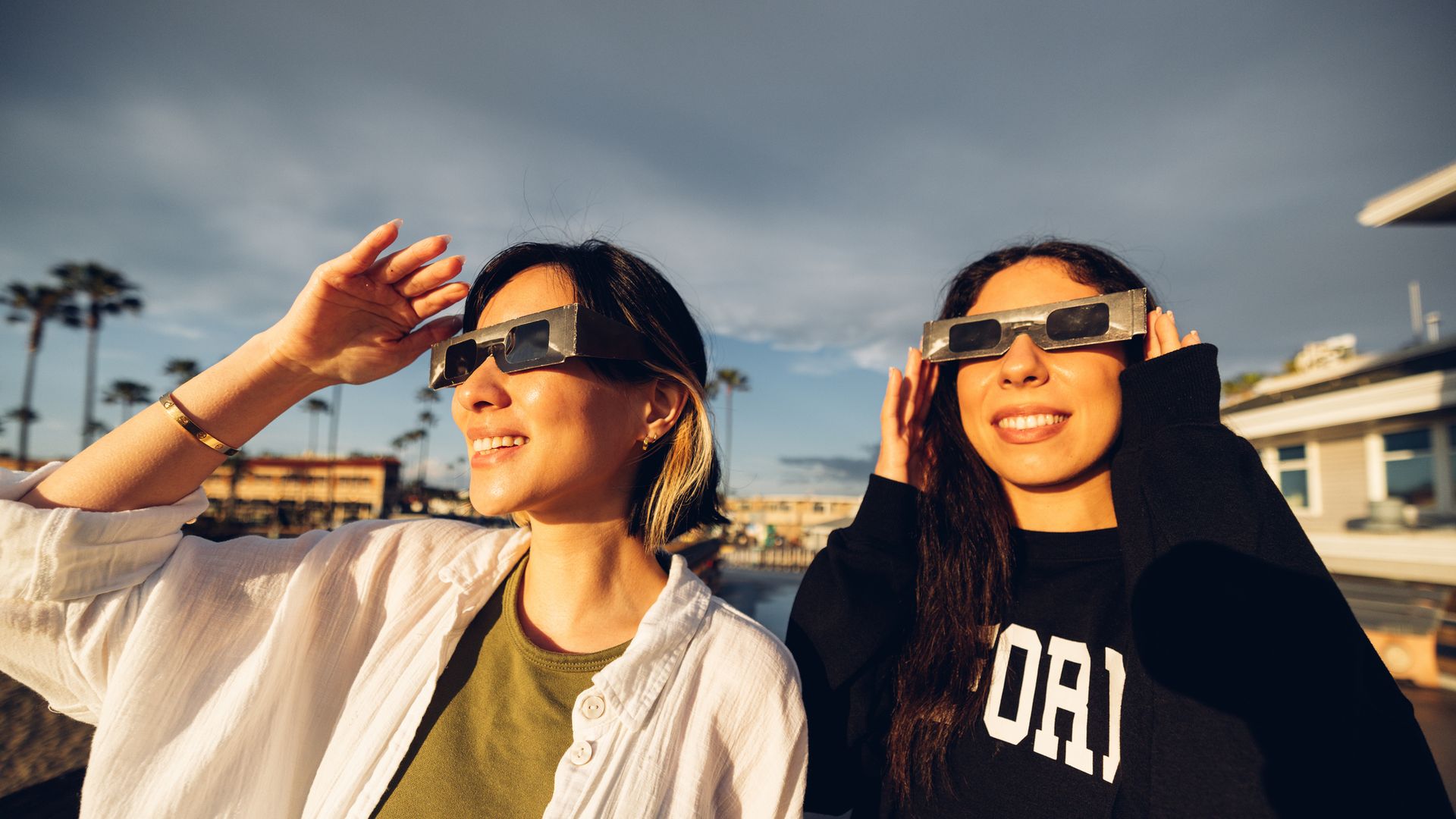 Dos chicas viendo un eclipse solar en algún hotel, cerca de la playa, mirando hacia el sol.