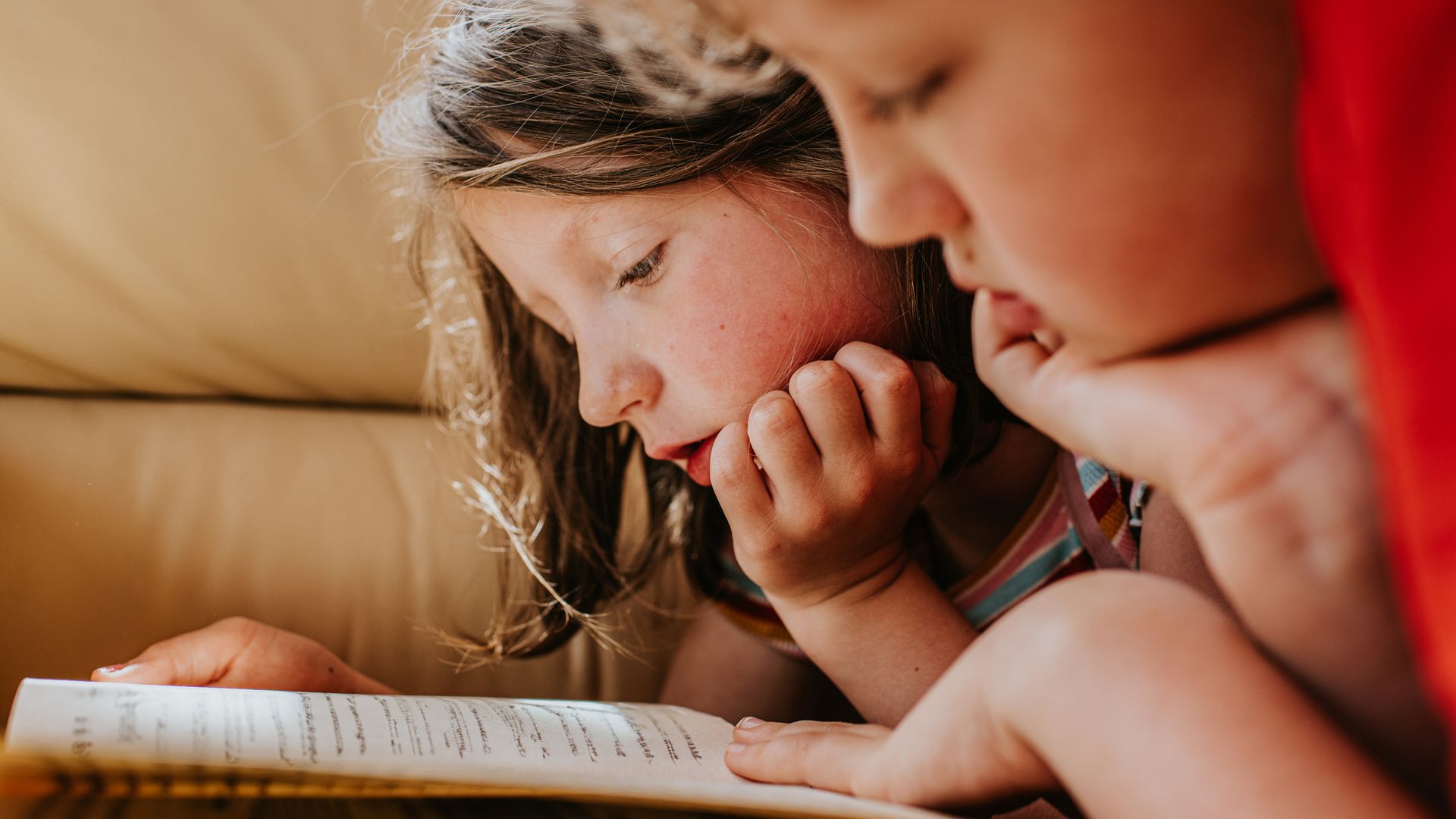 Dos niños tumbados boca abajo, leyendo y compartiendo un libro plenamente atentos.