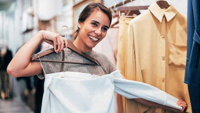 Mujer joven sonriendo y probándose una prenda en la tienda.