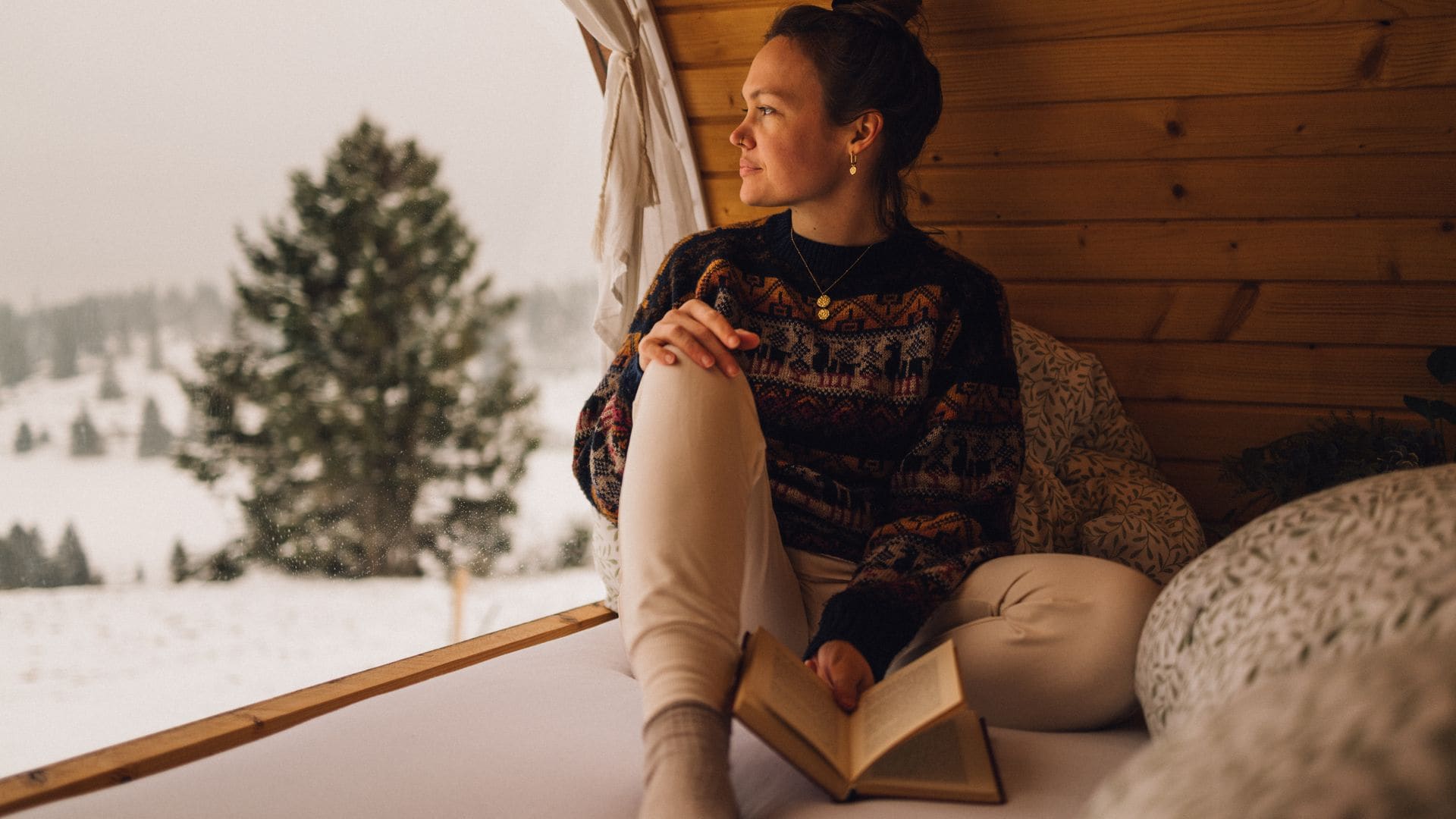 Una mujer mirando por la ventana con un libro