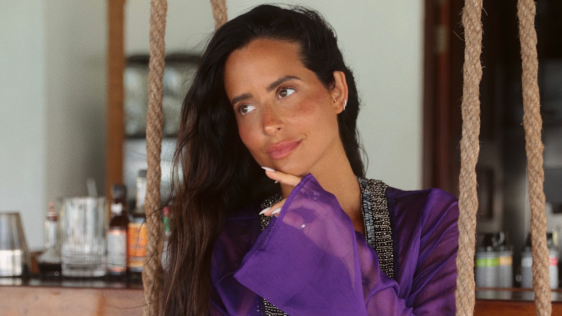 MARÍA FERNÁNDEZ-RUBÍES SOLER con vestido morado sentada en un columpio en un ambiente de verano