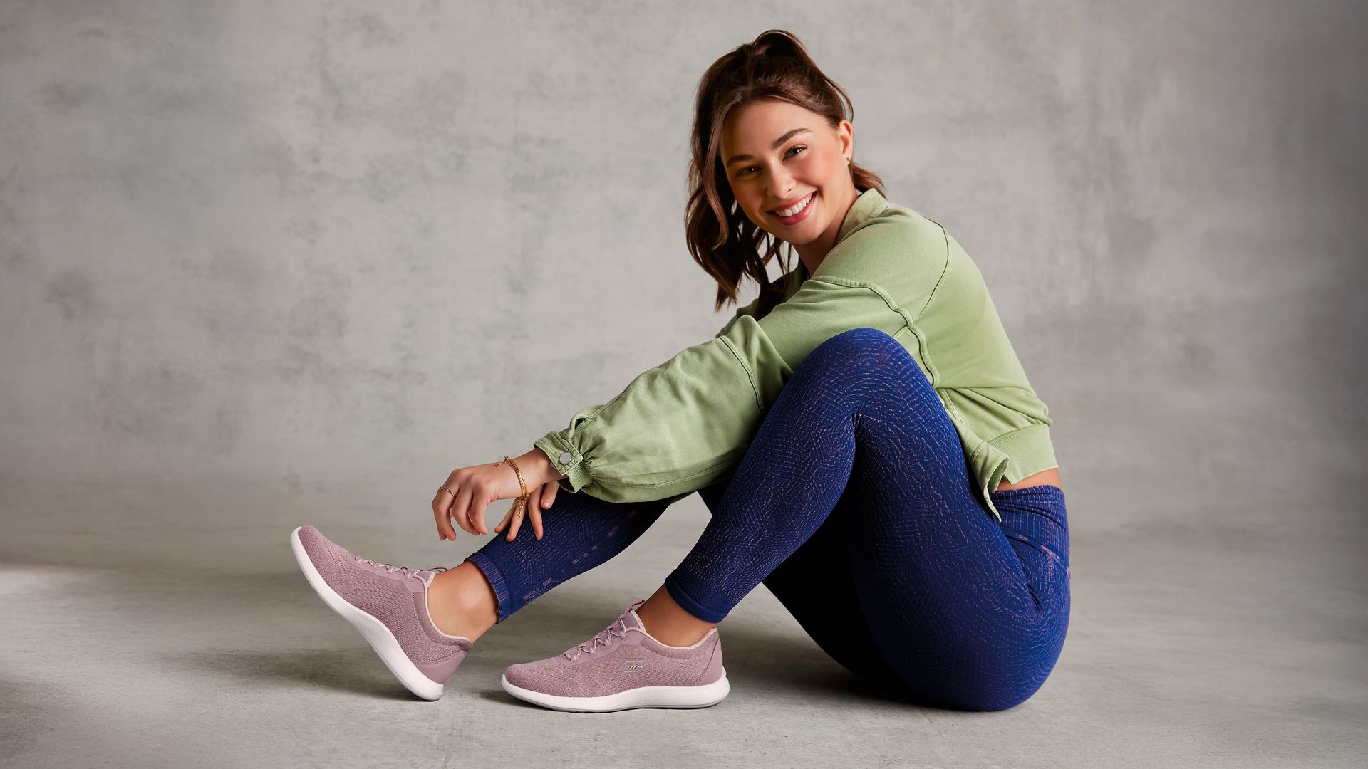 Mujer joven sentada en el suelo poniéndose unas zapatillas de Skechers