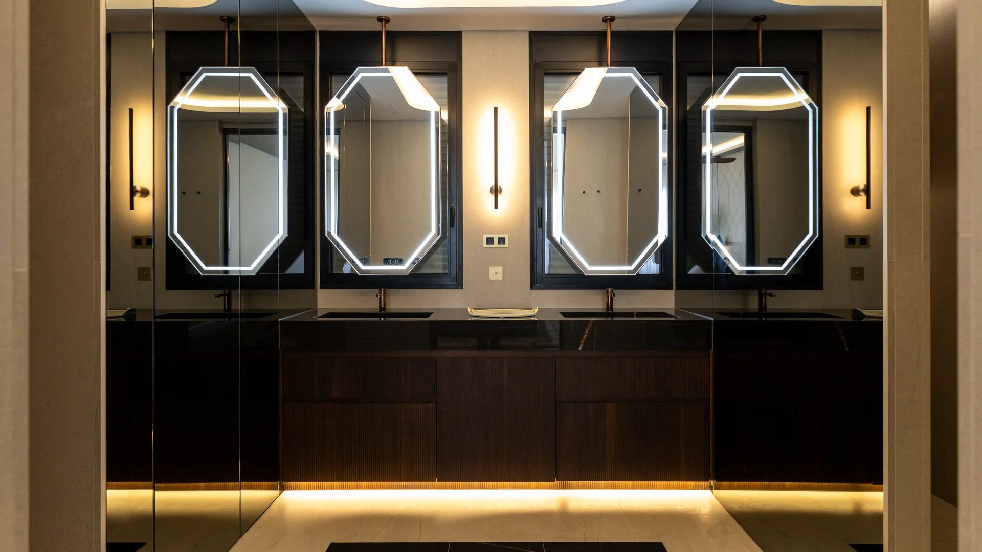 Baño con muebles oscuros, dos espejos retroiluminados, techo y suelo retroiluminado