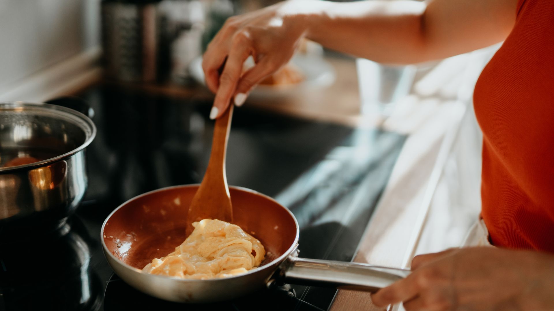 Mujer cocinando una tortilla en una sartén de acero inoxidable sobre la vitrocerámica en un plano detalle de la sartén y sus manos.