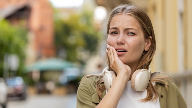 chica joven con dolor de muelas al aire libre, con unos auriculares grandes