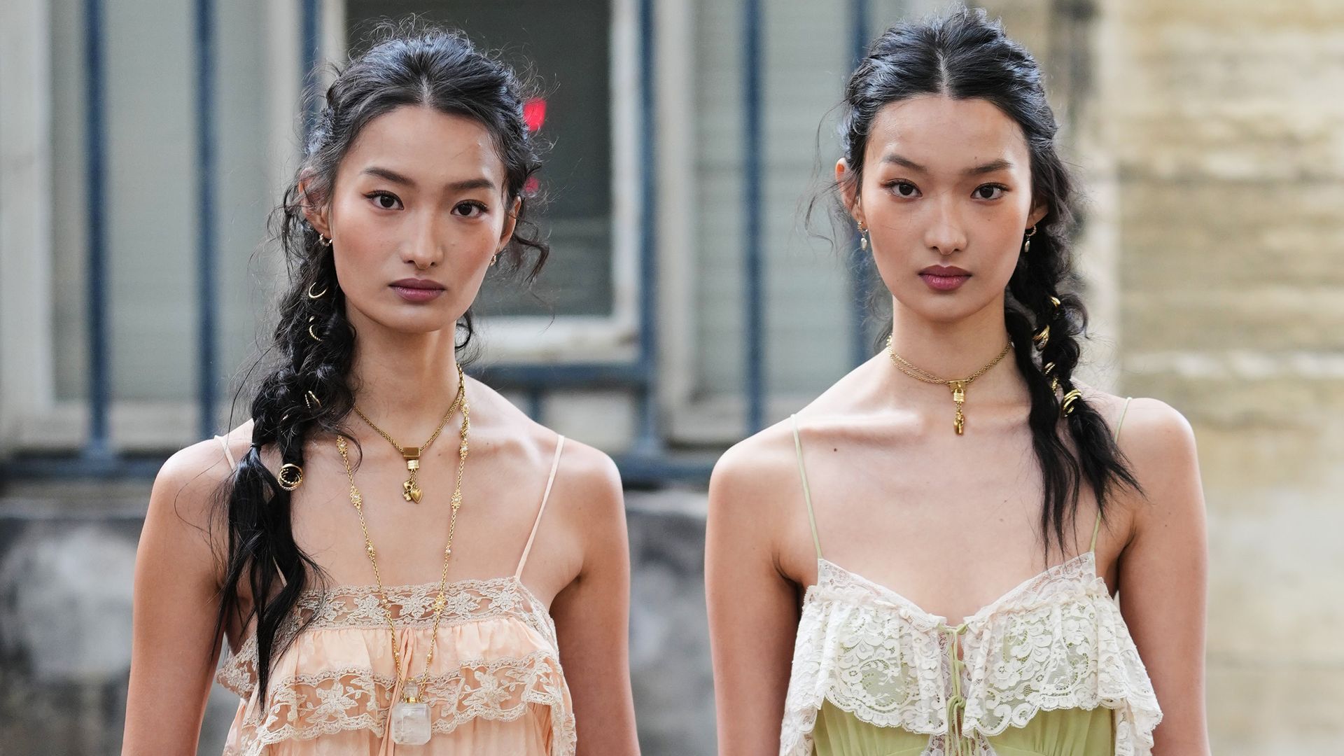 Dos chicas en la Semana de la Moda de París con vestido verde y otra rosa y trenzas adornadas con anillas