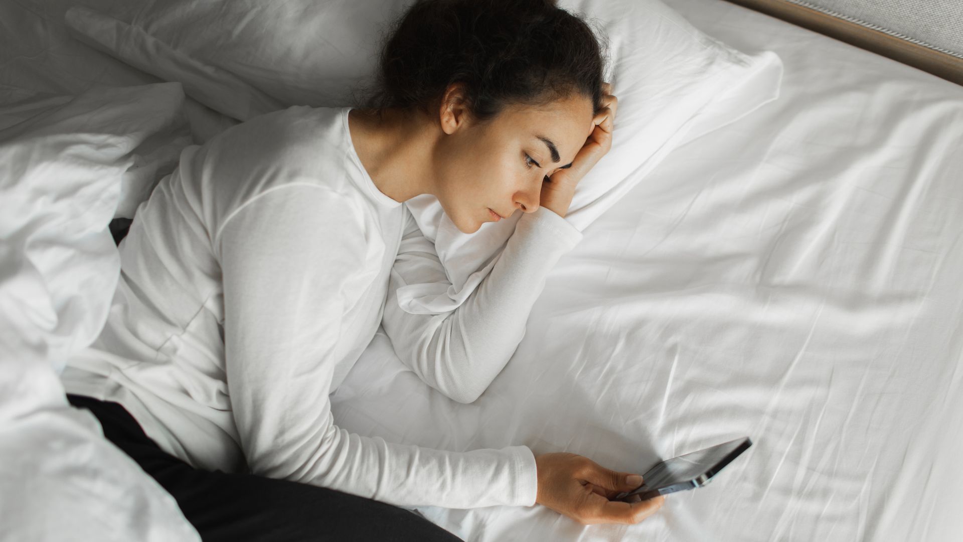 mujer en la cama, despierta mirando el móvil, sin poder dormir