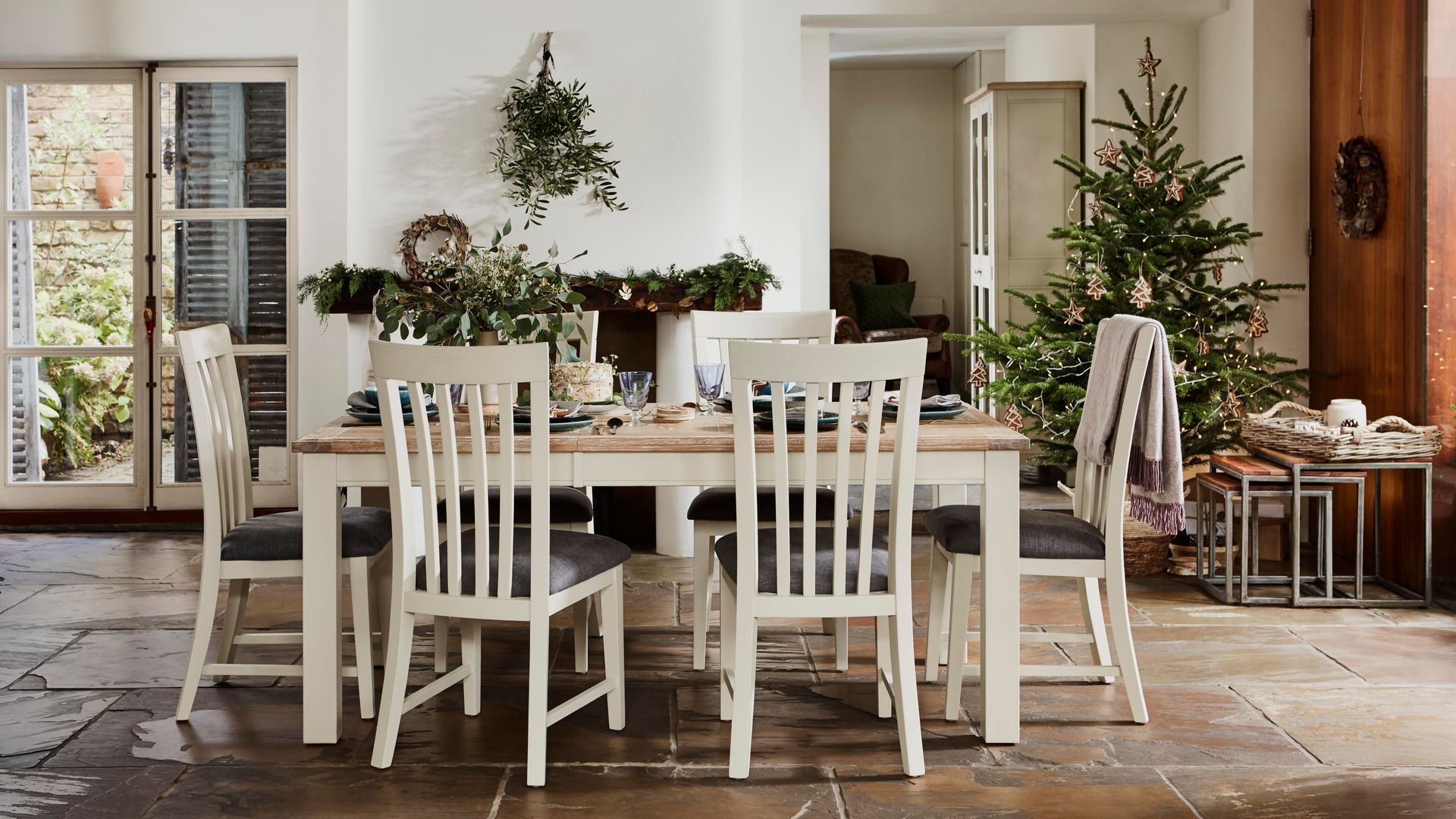 Comedor con chimenea, mesa de Navidad con sillas blancas, mesa blanca con el sobre de madera, árbol de Navidad, vigas de madera en el techo, suelo porcelanico