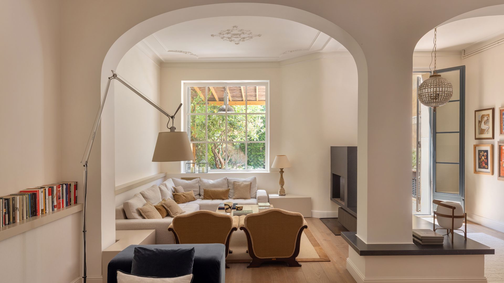 Salón XL con salida al jardín, arcos separando el estar del rincón de lectura, lámpara de pie, sofás blancos, butaca azul 