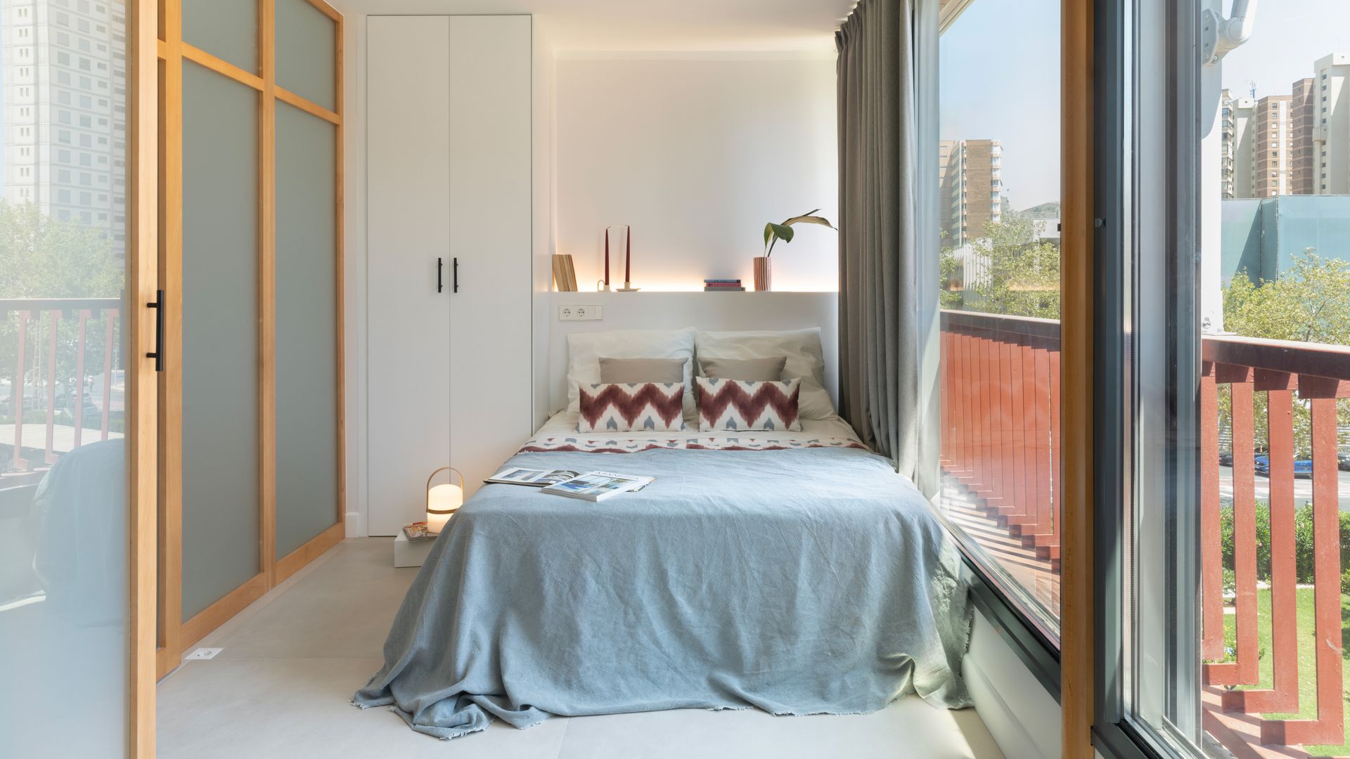 Dormitorio con ventanales y salida a balcón, cabecero de obra con luz, ropa de cama azul, lámpara Cesta en el suelo. puertas de madera con cristales al ácido