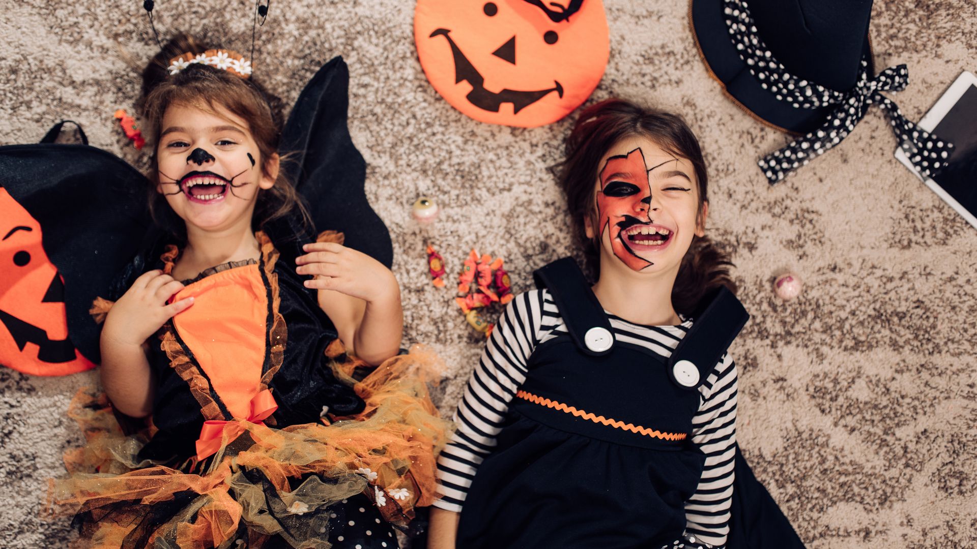 Niñas riendo tumbadas en el suelo con su disfraz de Halloween en negro y naranja.