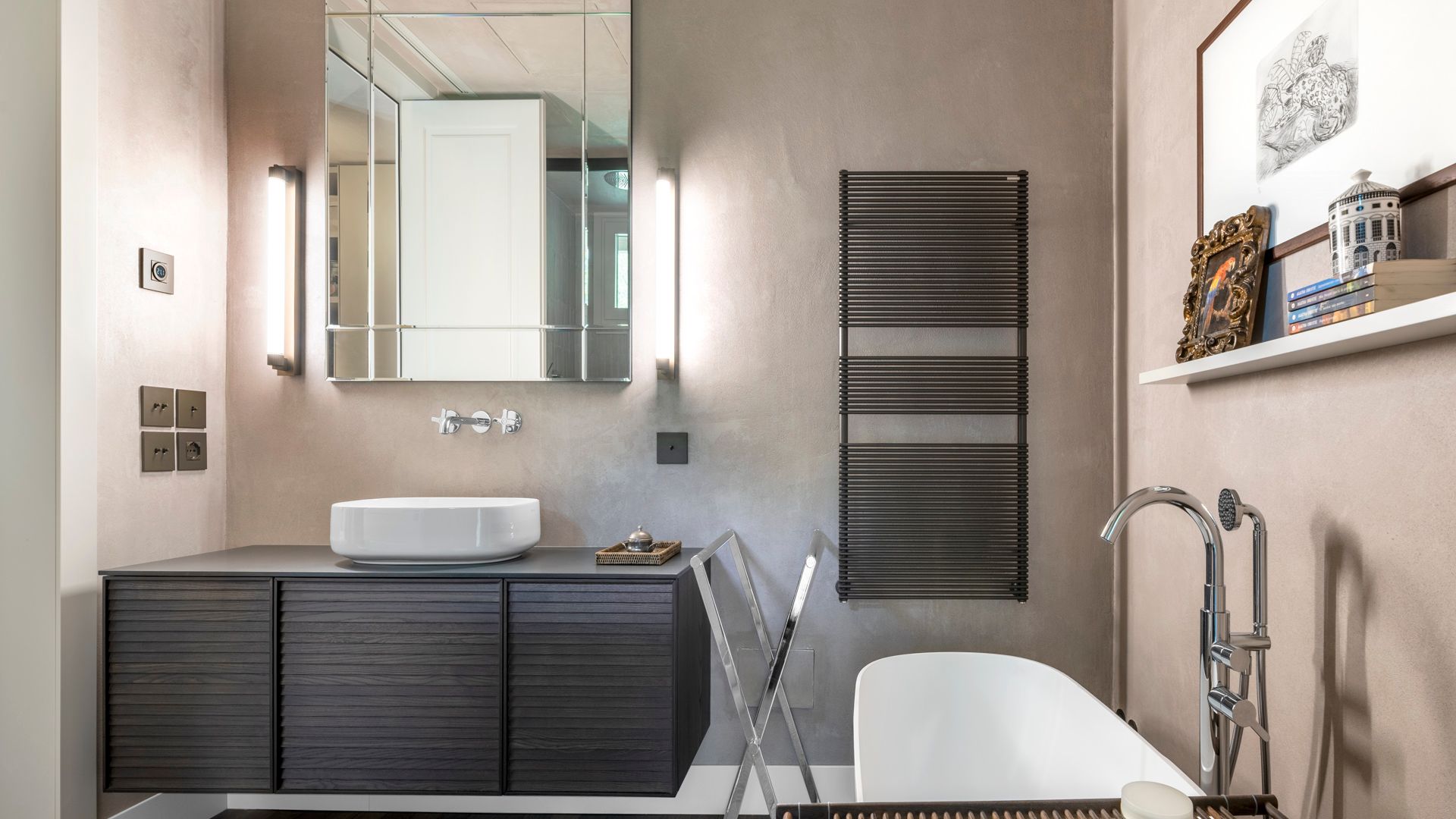 Baño con bañera exenta, espejo, mueble negro, repisa con cuadros, radiador toallero