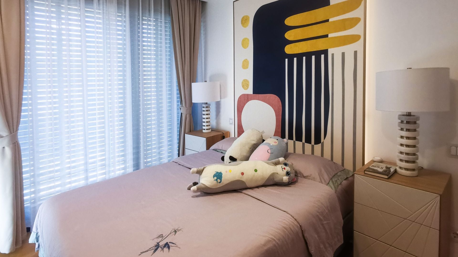 Dormitorio infantil con cortinas y visillos, cuadro en la pared del cabecero, ropa de cama rosa y cojines con formas de animales