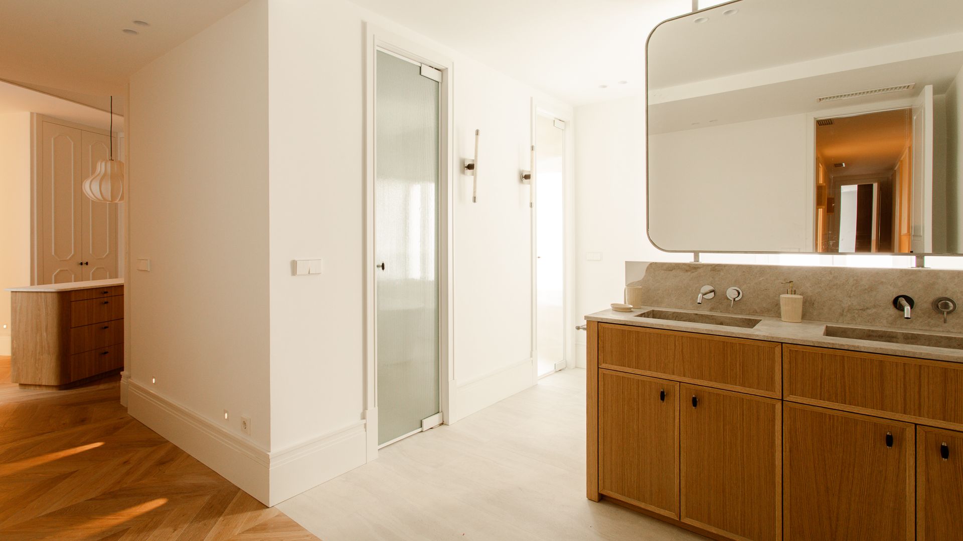 Baño grande con el inodoro independiente tras una puerta de cristal, espejo XL que cuelga del techo, mueble de madera con dos lavabos 