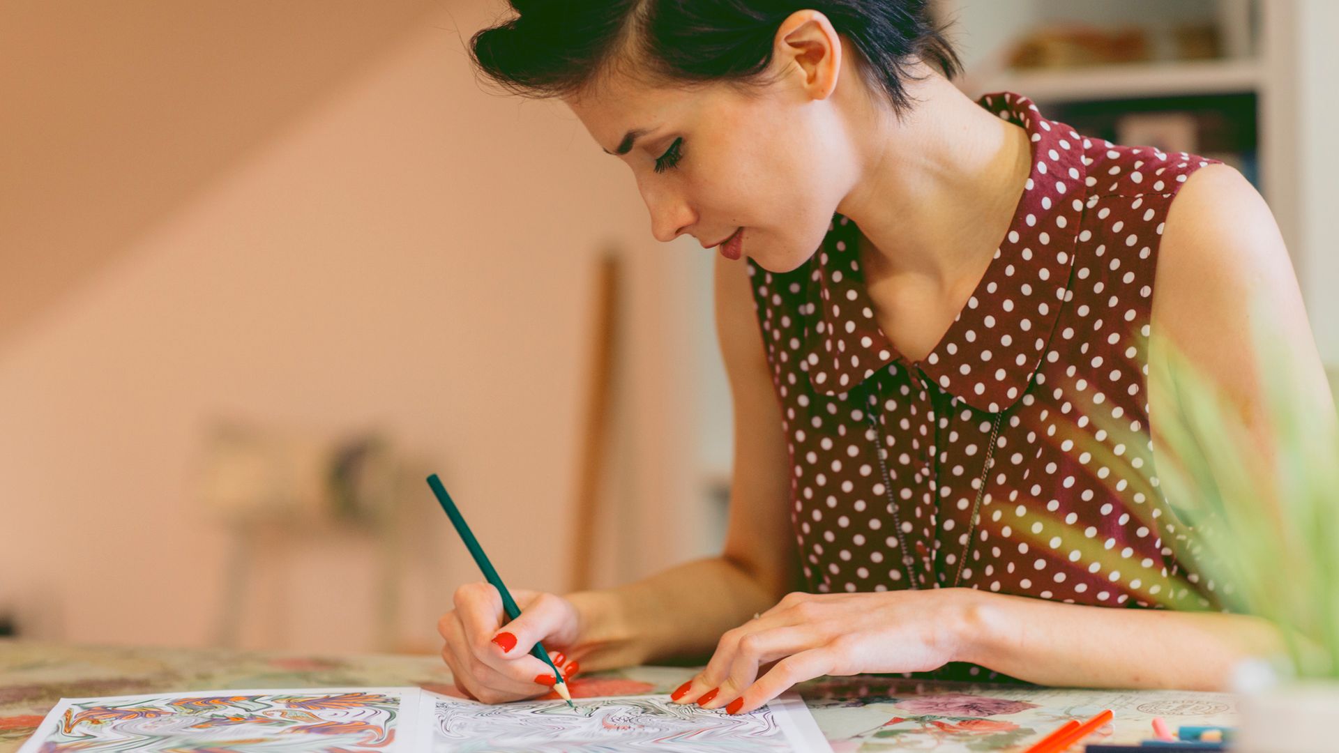 Mujer coloreando mandalas en un cuaderno, con lápices de colores encima de la mesa-