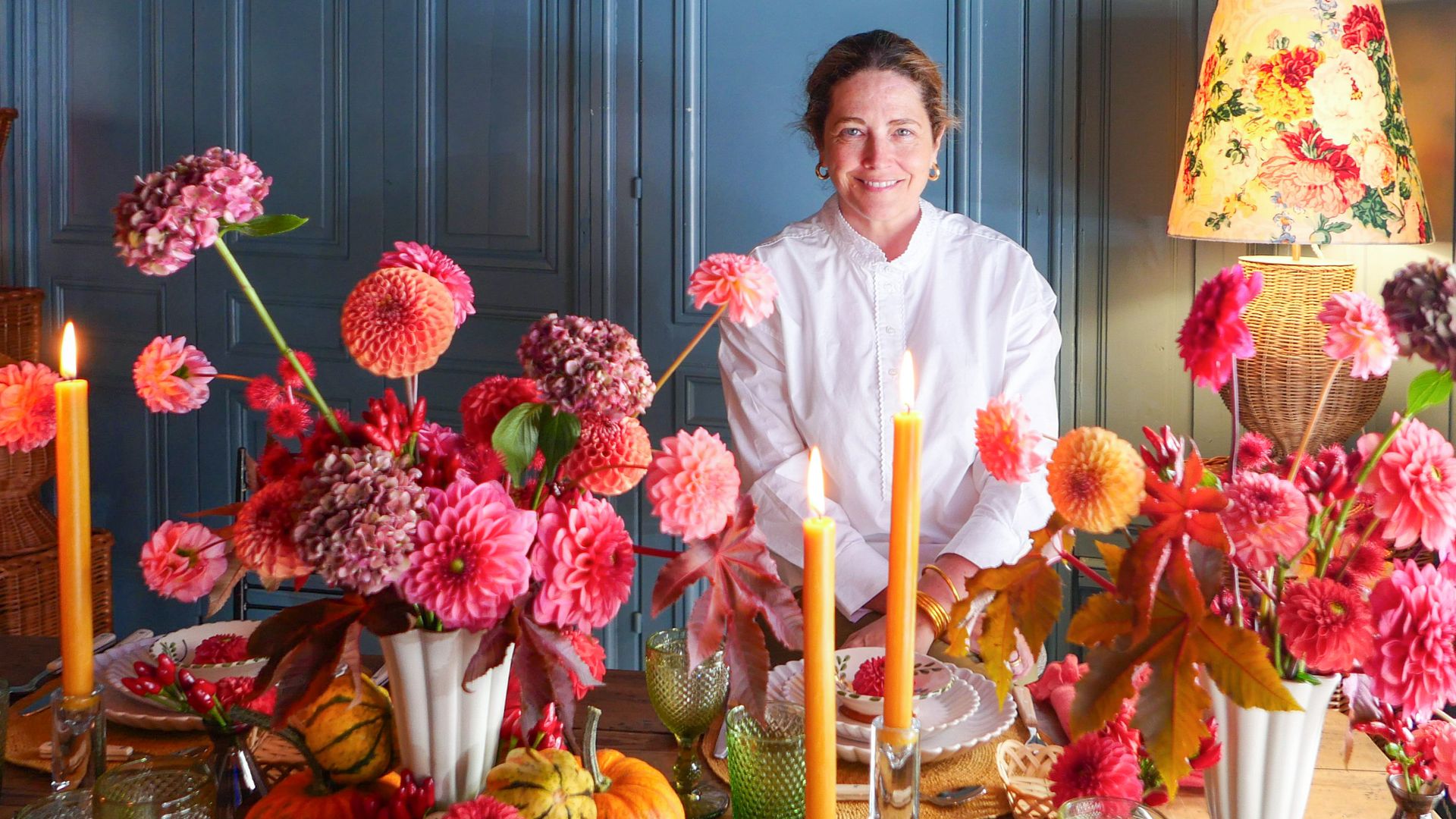 Retrato de la diseñadora floral, Sally Hambleton con una mesa con arreglos florales y calabazas