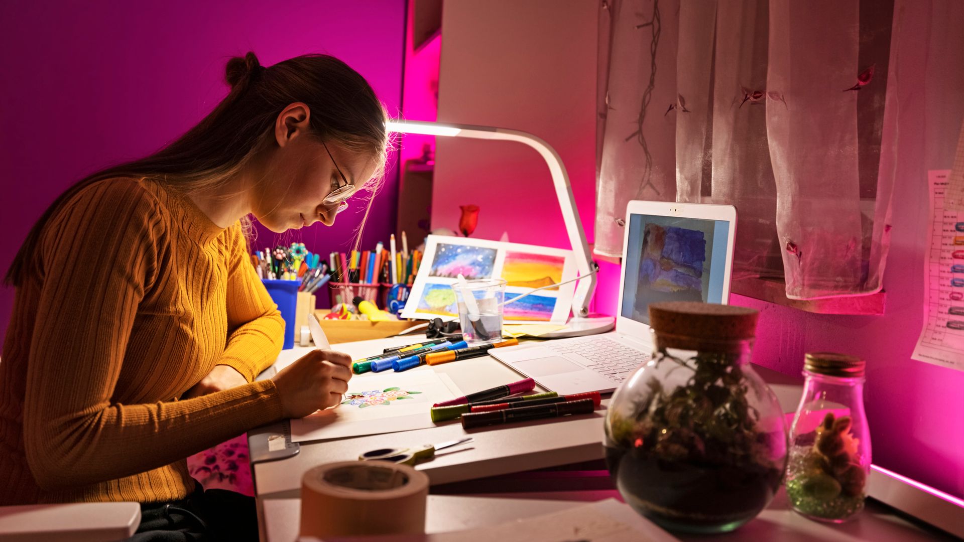 Chica joven o adolescente pintando dibujos en su habitación, en el escritorio con una lámpara y su colección de rotuladores sobre la mesa.