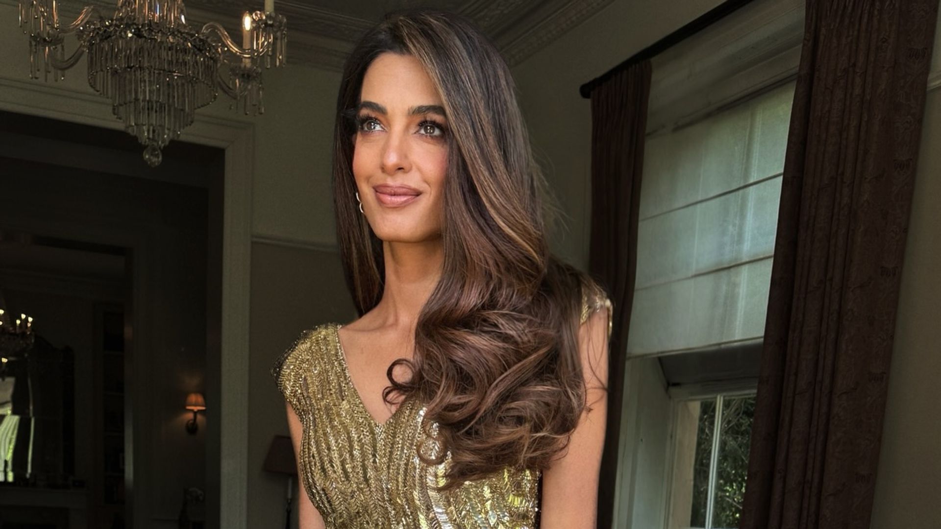 Amal Clooney en su casa con vestido dorado de Alexander McQueen y pelo suelto