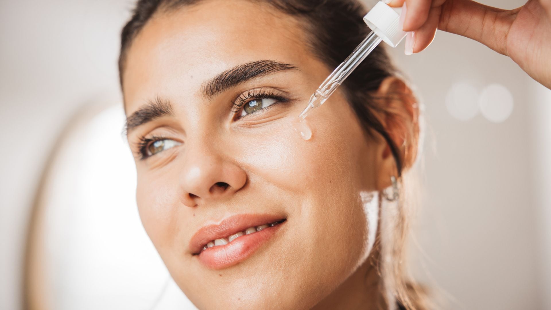 Rostro de mujer joven aplicándose sérum facial con pipeta