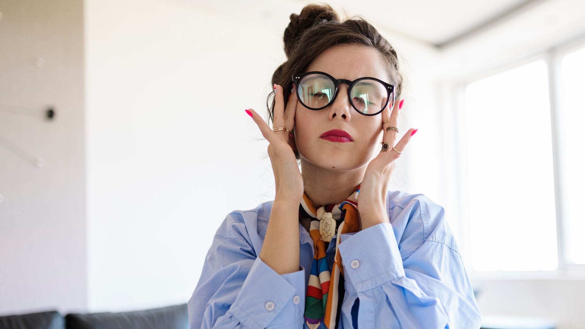 Mujer masajeando sus sienes en la oficina, con gafas y dolor de cabeza.