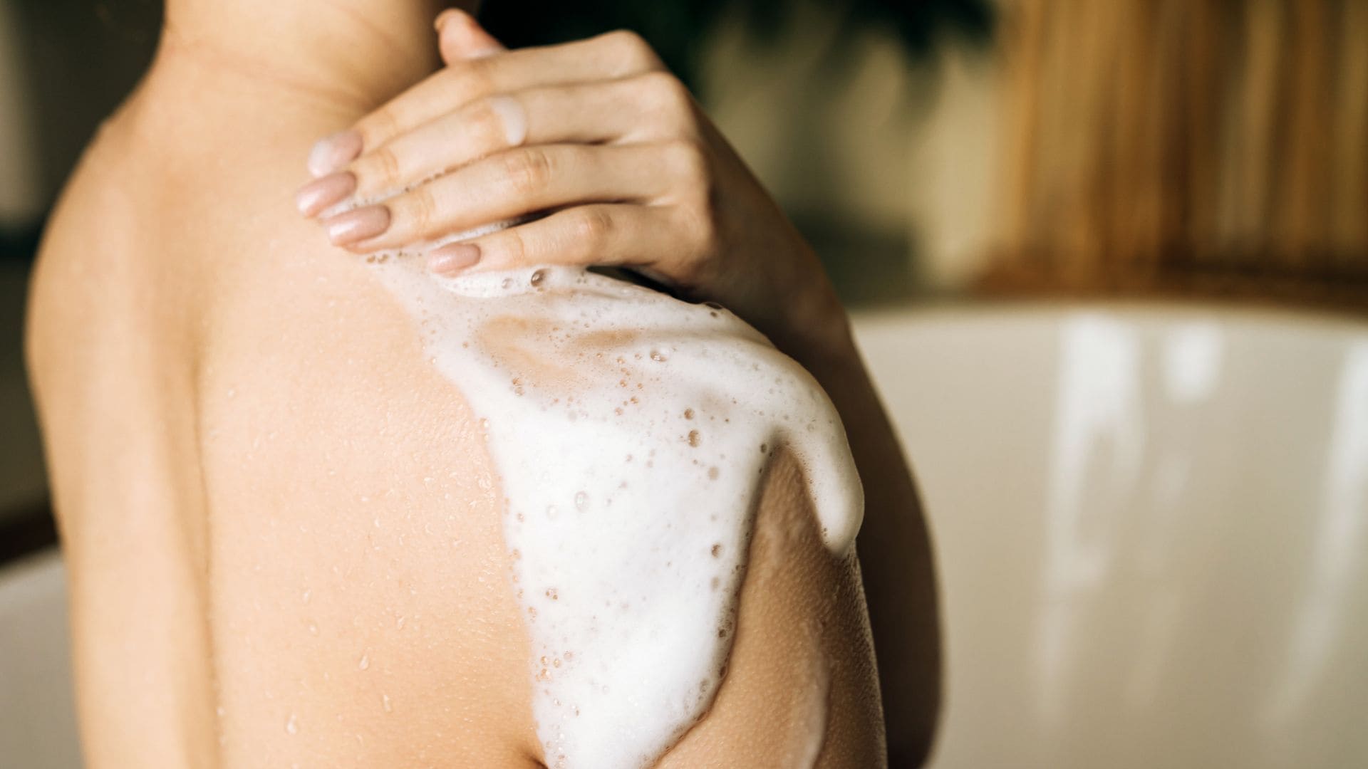 Mujer enjabonándose con la mano en el hombro y espuma de jabón, en una imagen solo del cuello a media espalda.