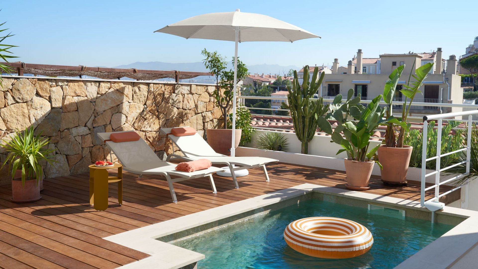 Terraza con piscina con sombrilla blanca, tumbonas blancas, suelo de madera, plantas