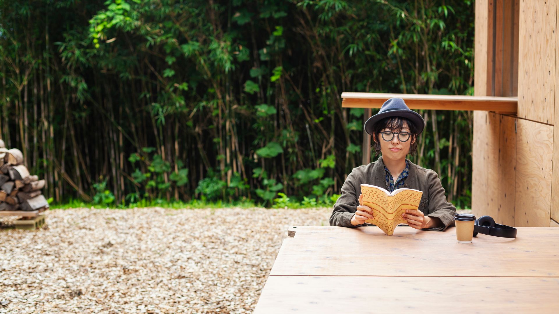 Mujer japonesa con ropa de otoño-invierno a las afueras de una cabaña de madera en medio del bosque leyendo un libro o cuaderno.