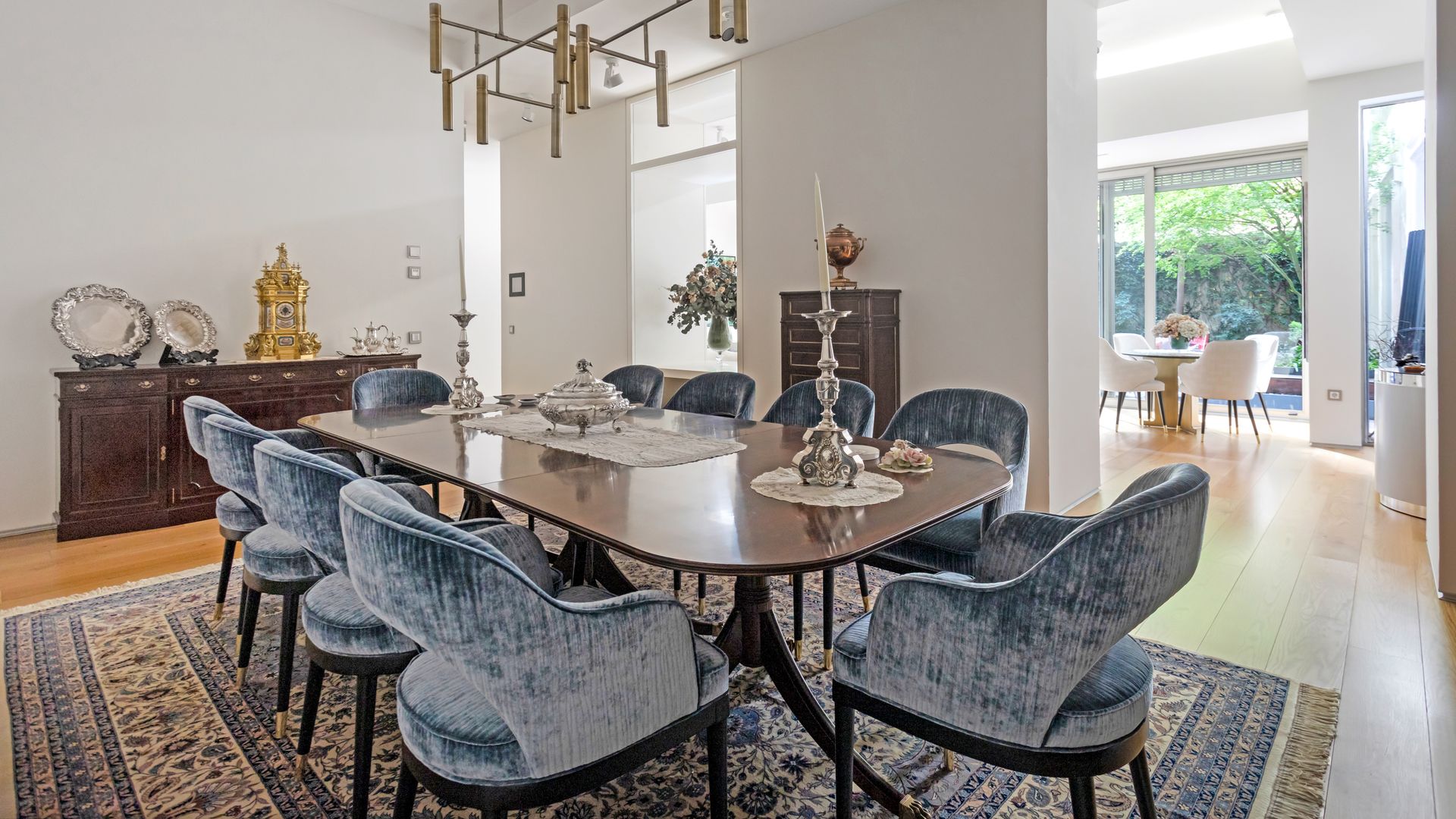 Comedor formal con mesa de madera, aparador de madera oscura, sillas de comedor tapizadas, alfombra, candelabros, lámpara de techo
